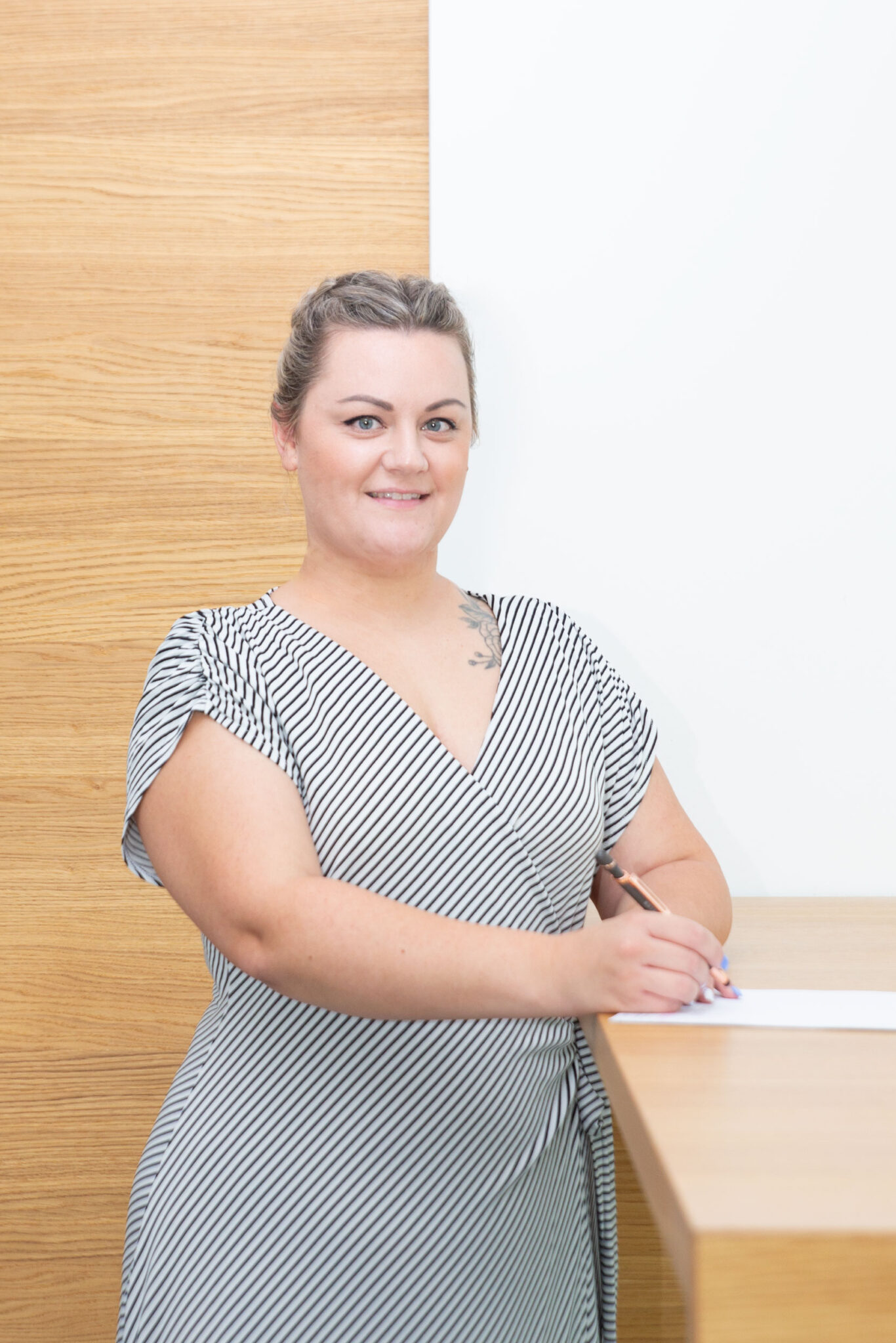 Eine Frau in einem gestreiften Kleid steht an einem Tisch und schreibt mit einem Stift auf einem Blatt Papier.