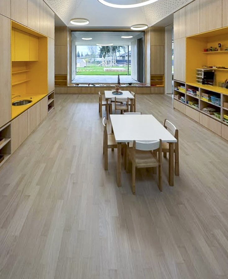 Innenraum eines Kindergartens mit hellen Holzmöbeln, Tischen und Regalen.