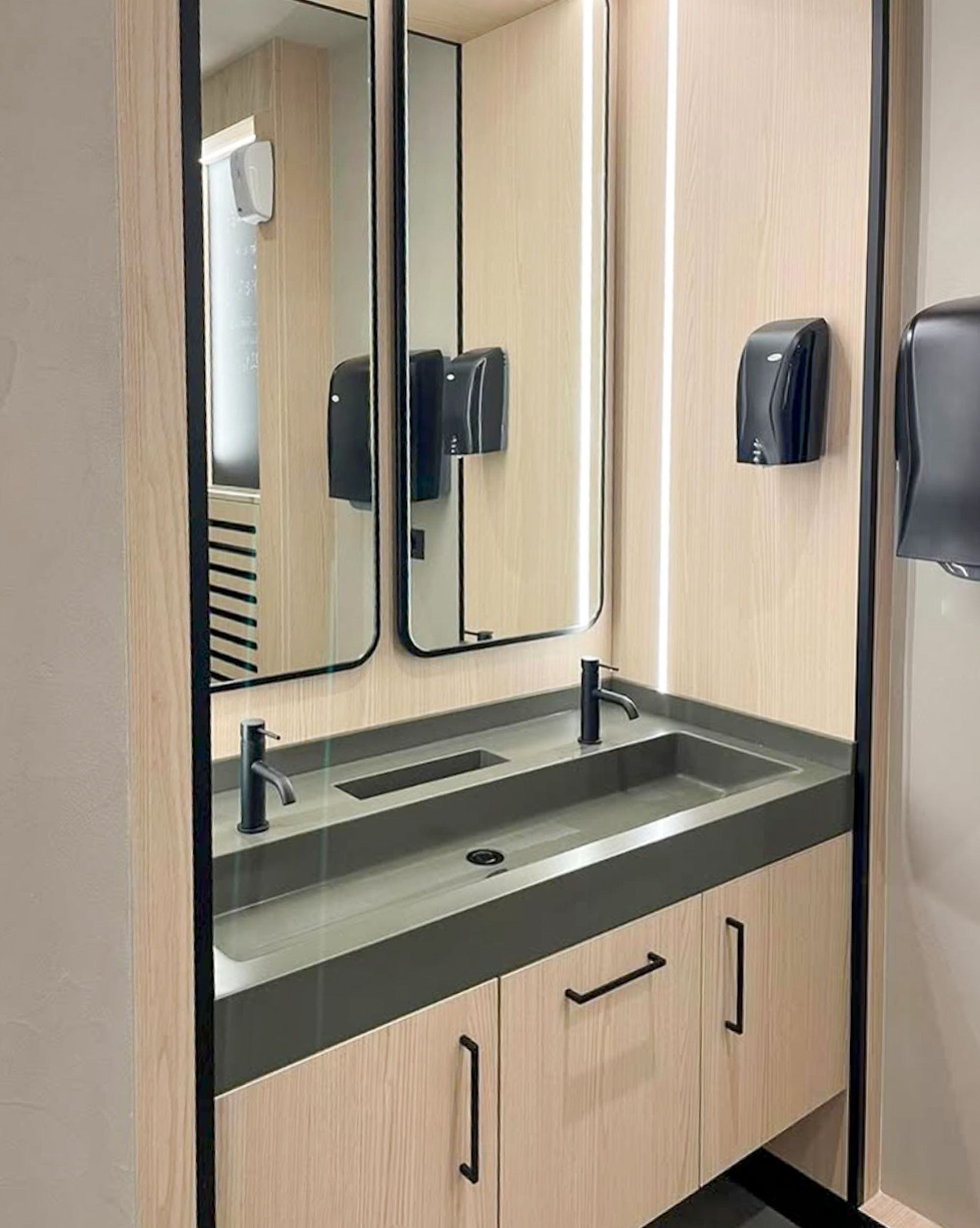 Moderne Badezimmerausstattung mit einem grauen Waschbecken und zwei großen Spiegeln an der Wand.