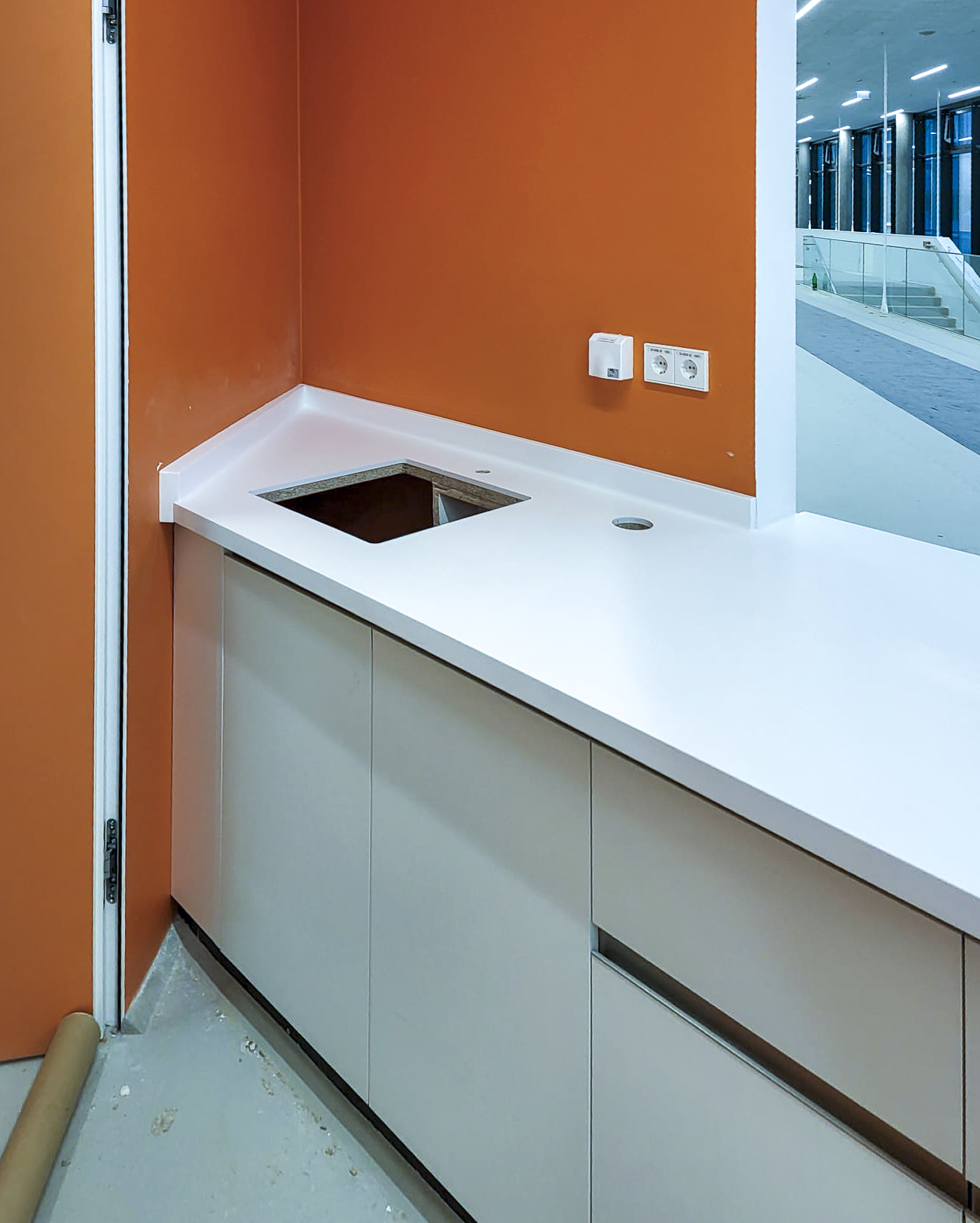 Weiße Küchenarbeitsplatte mit integriertem Spülbecken und orangefarbener Wand im Hintergrund.