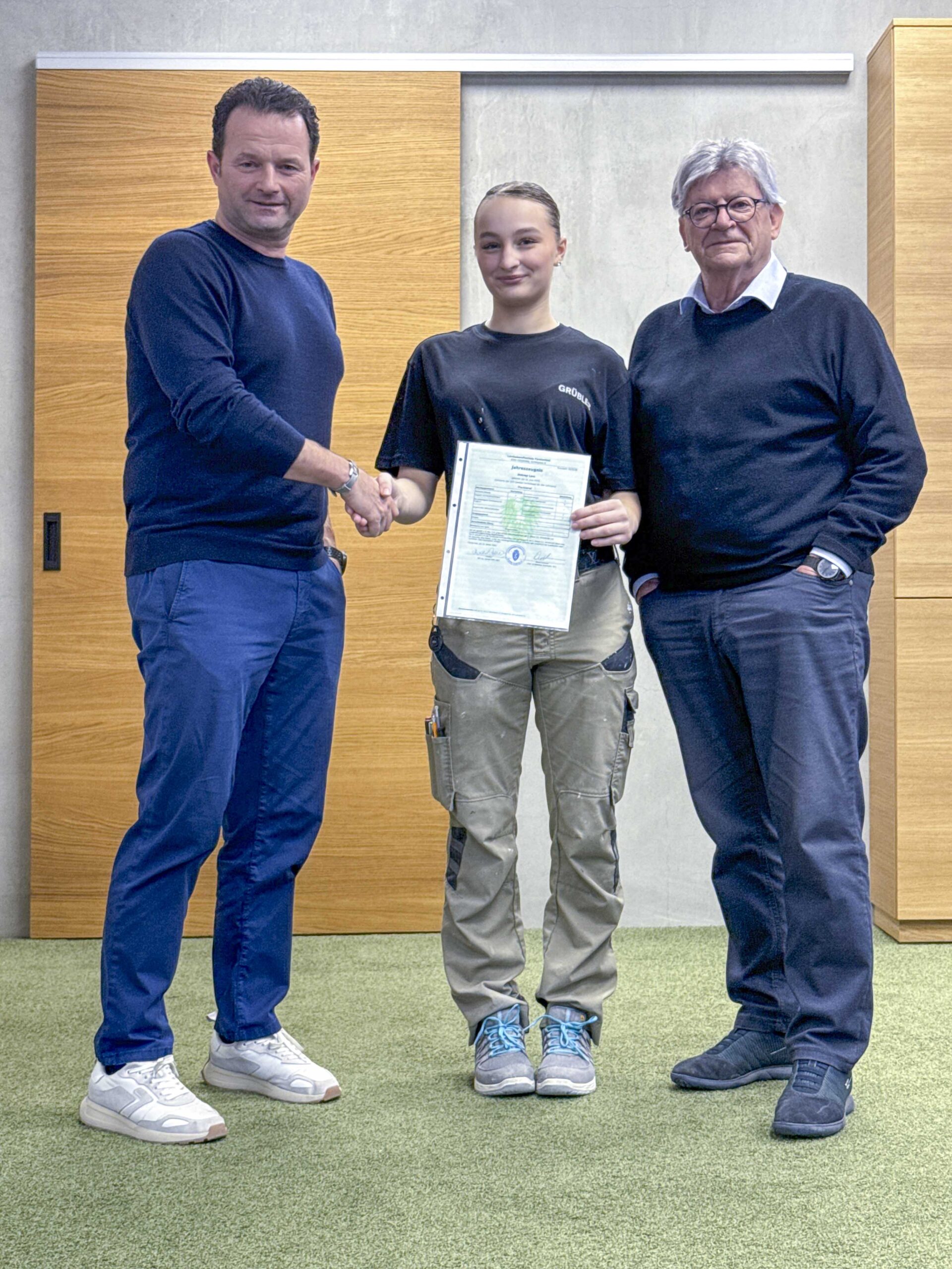 Zwei Männer und eine Frau stehen zusammen und halten ein Zertifikat in der Hand, während sie sich die Hand schütteln.